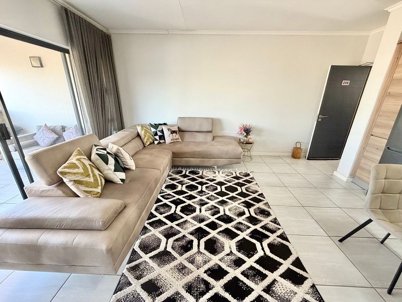 A bright living room featuring neutral tiled flooring, a large sliding glass door providing access to the balcony, and clean, modern finishes.