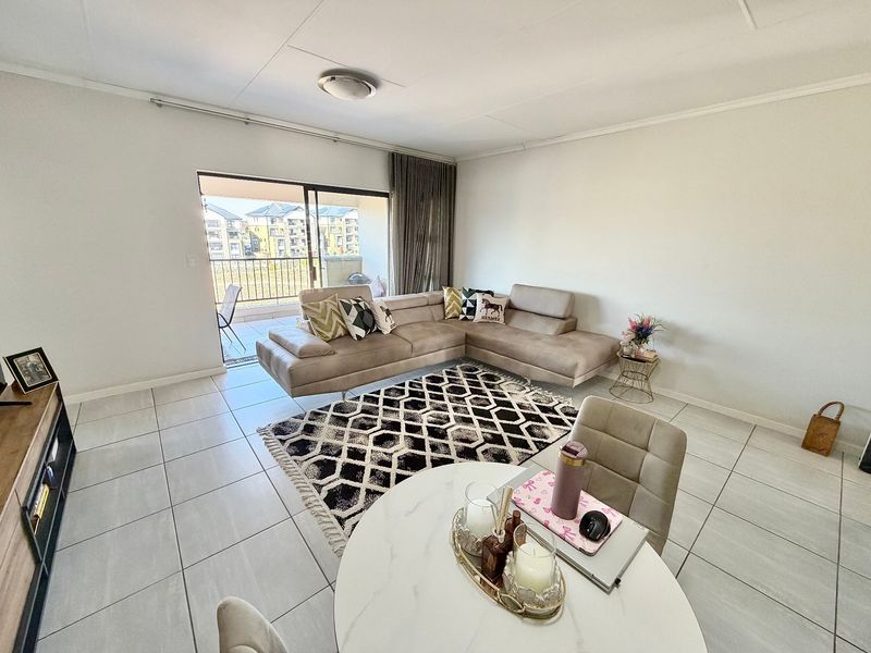 Bright open-plan living area featuring neutral tiled flooring and direct access to a private balcony through sliding glass doors.