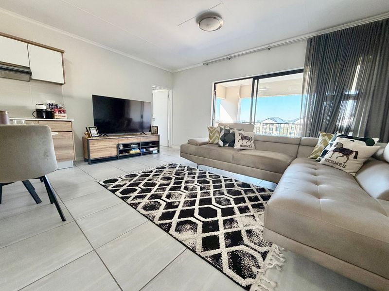 Bright open-plan living area featuring tiled floors, modern kitchen cabinetry, and a large sliding door leading to a balcony.