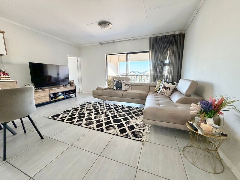 A bright and spacious living room featuring large format floor tiles and a sliding glass door providing access to an outdoor balcony area.