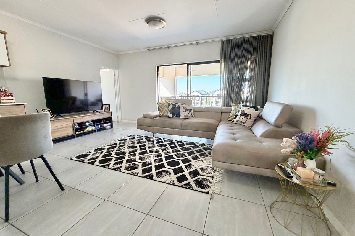 A bright and spacious living room featuring large format floor tiles and a sliding glass door providing access to an outdoor balcony area.