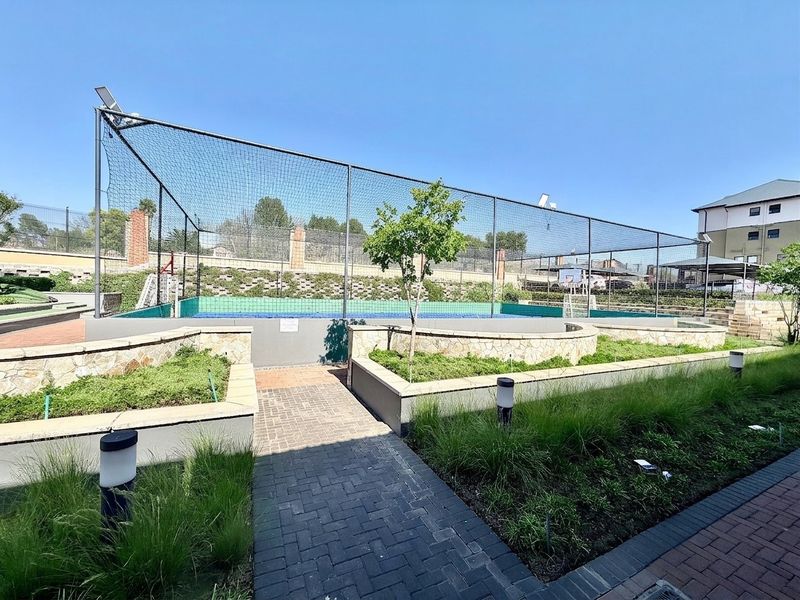 A well-maintained outdoor sports facility featuring a fenced court, paved pathways, and landscaped garden beds within the apartment complex.