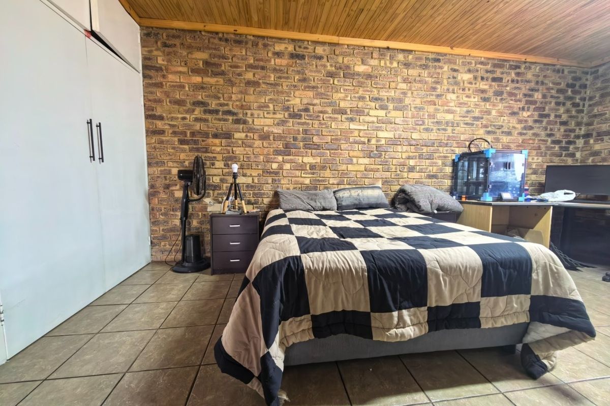 A bedroom featuring an exposed brick feature wall, timber ceiling, tiled flooring, and a built-in wardrobe.