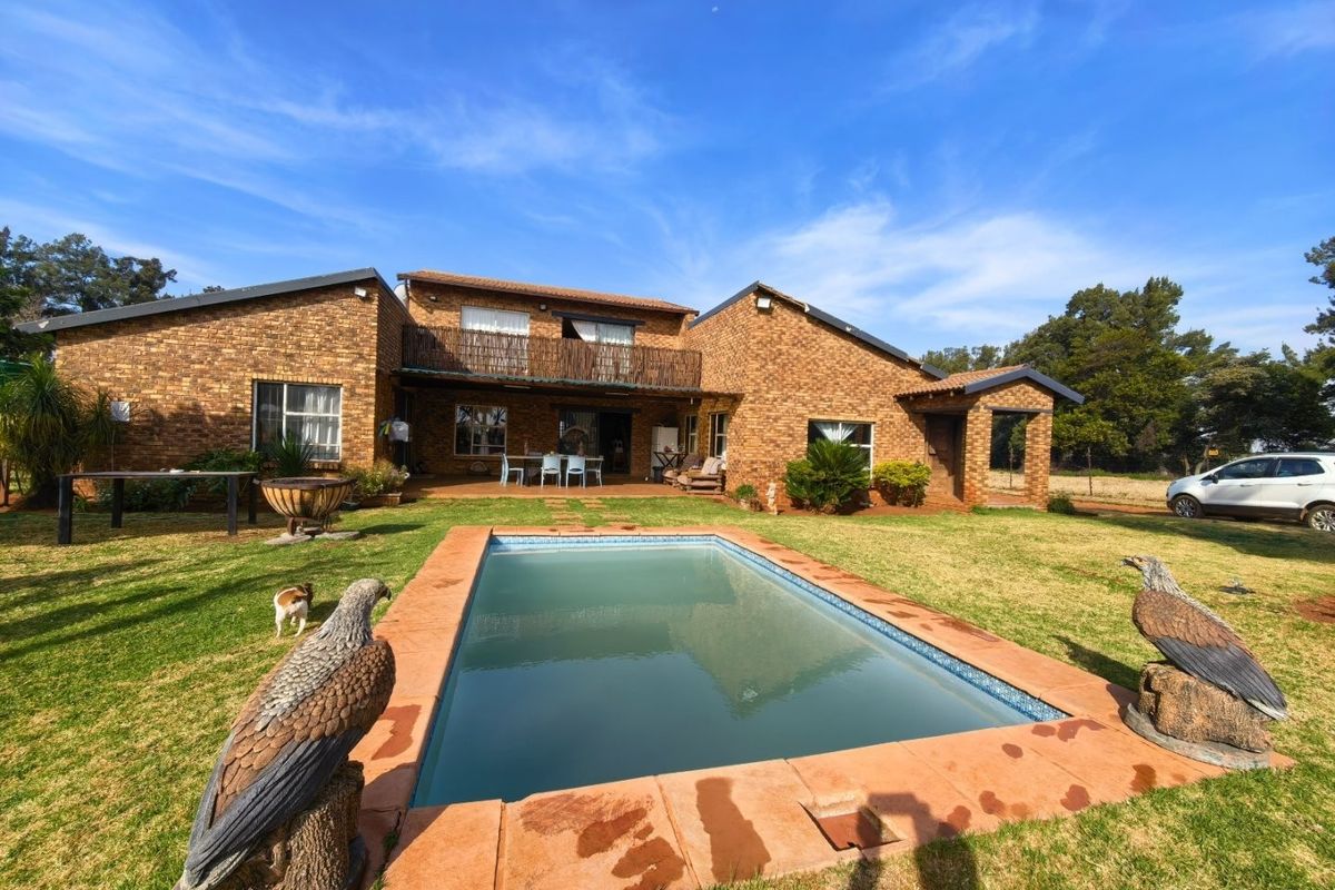 Rear view of a double-story brick house featuring a swimming pool, a covered patio area, and a balcony overlooking the garden.
