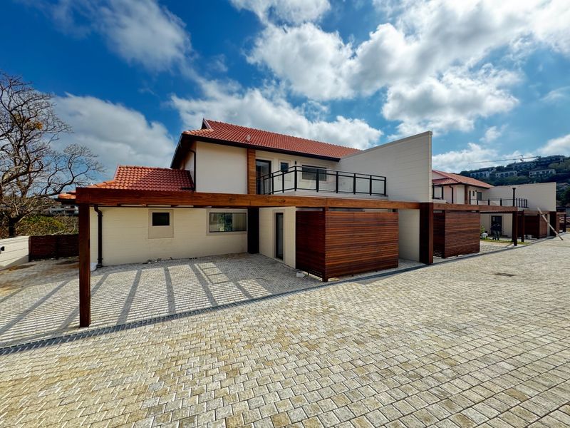 Front exterior view of a modern townhouse featuring a paved driveway, timber pergola, and a private balcony with glass balustrades.