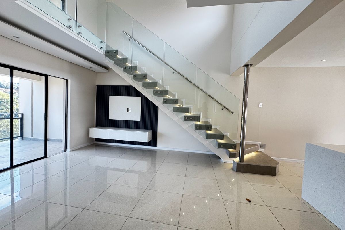 Modern open-plan living area featuring a striking floating staircase with glass balustrades, sleek porcelain tiling, and a contemporary built-in media wall.