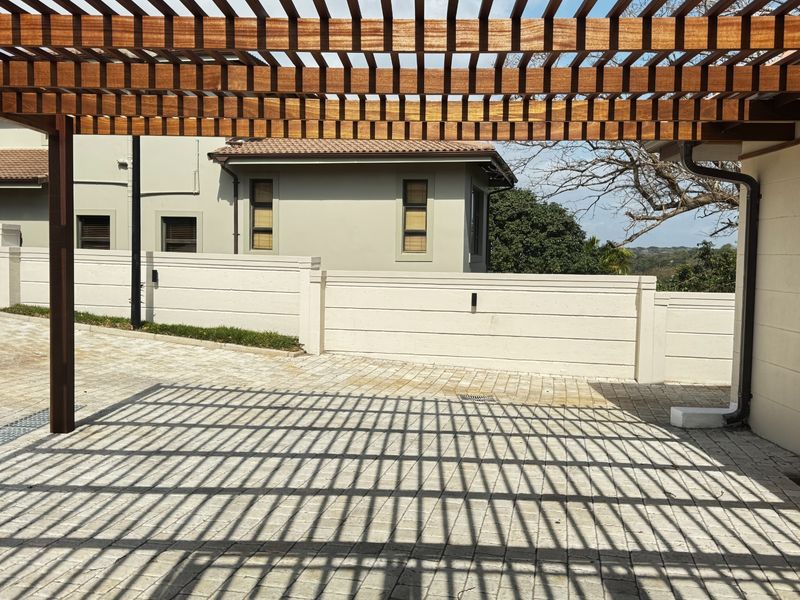 A well-maintained outdoor area featuring a timber pergola providing shade over a paved driveway and boundary wall.