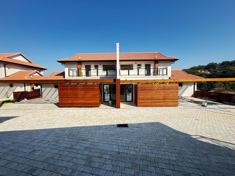 Front elevation of a modern townhouse featuring terracotta roof tiles, timber privacy screens, a paved driveway, and an upper-level balcony.