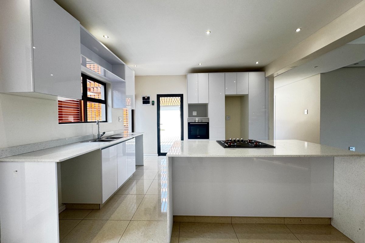 Modern kitchen featuring sleek white gloss cabinetry, quartz countertops, a central island with a gas hob, and integrated oven, finished with polished floor tiles.