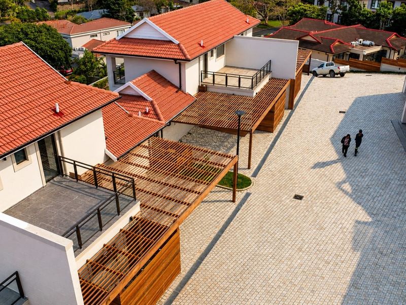 Aerial view of a townhouse complex featuring terracotta tiled roofs, timber pergolas, and a paved communal driveway area.