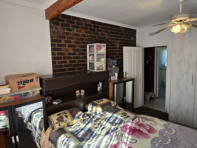 Bedroom featuring an exposed brick feature wall, timber ceiling beam, built-in cupboards, and a ceiling fan.