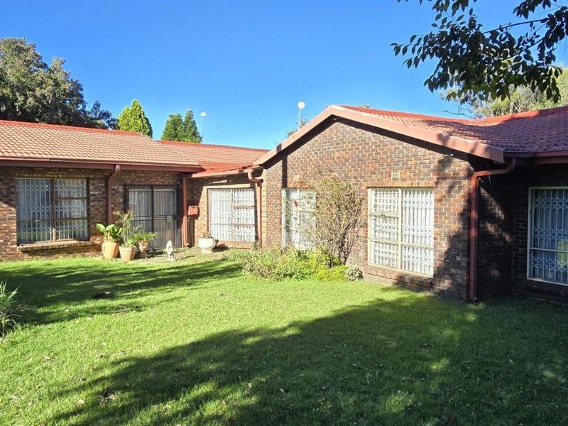 Rear view of a face brick house featuring a tiled roof, security bars on windows, and a well-maintained lawn area.