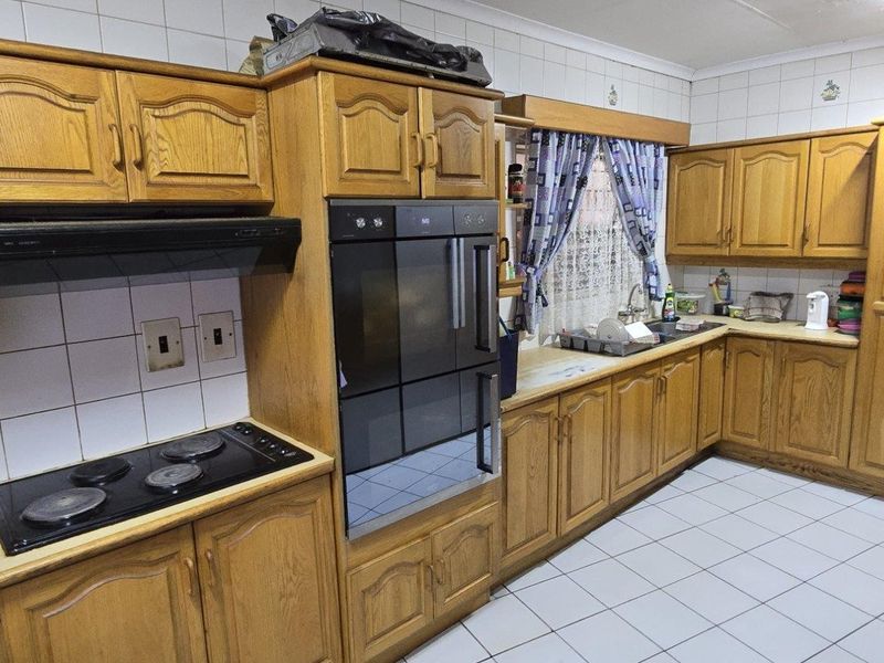 A functional kitchen featuring traditional wooden cabinetry, built-in oven and hob, tiled splashbacks, and tiled flooring, offering a classic layout with ample storage space.