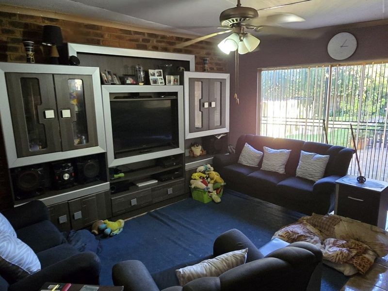 A living room featuring an exposed brick wall, ceiling fan, and sliding glass door access to the outdoor area.