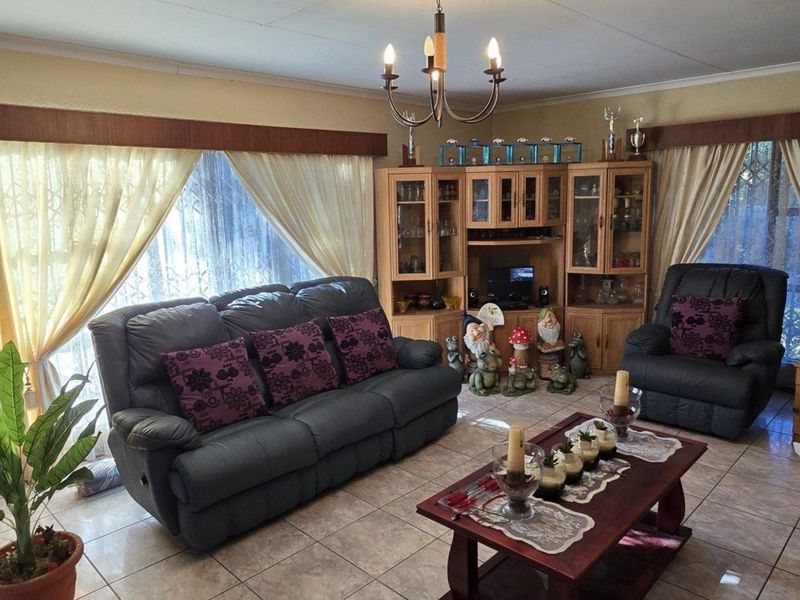 A living room featuring tiled flooring, built-in wooden cabinetry, and a central light fixture, with visible ceiling cracks requiring attention.