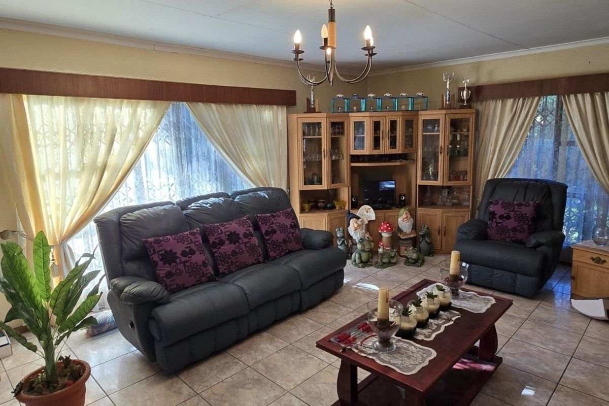 A living room featuring tiled flooring, built-in wooden cabinetry, and a central light fixture, with visible ceiling cracks requiring attention.
