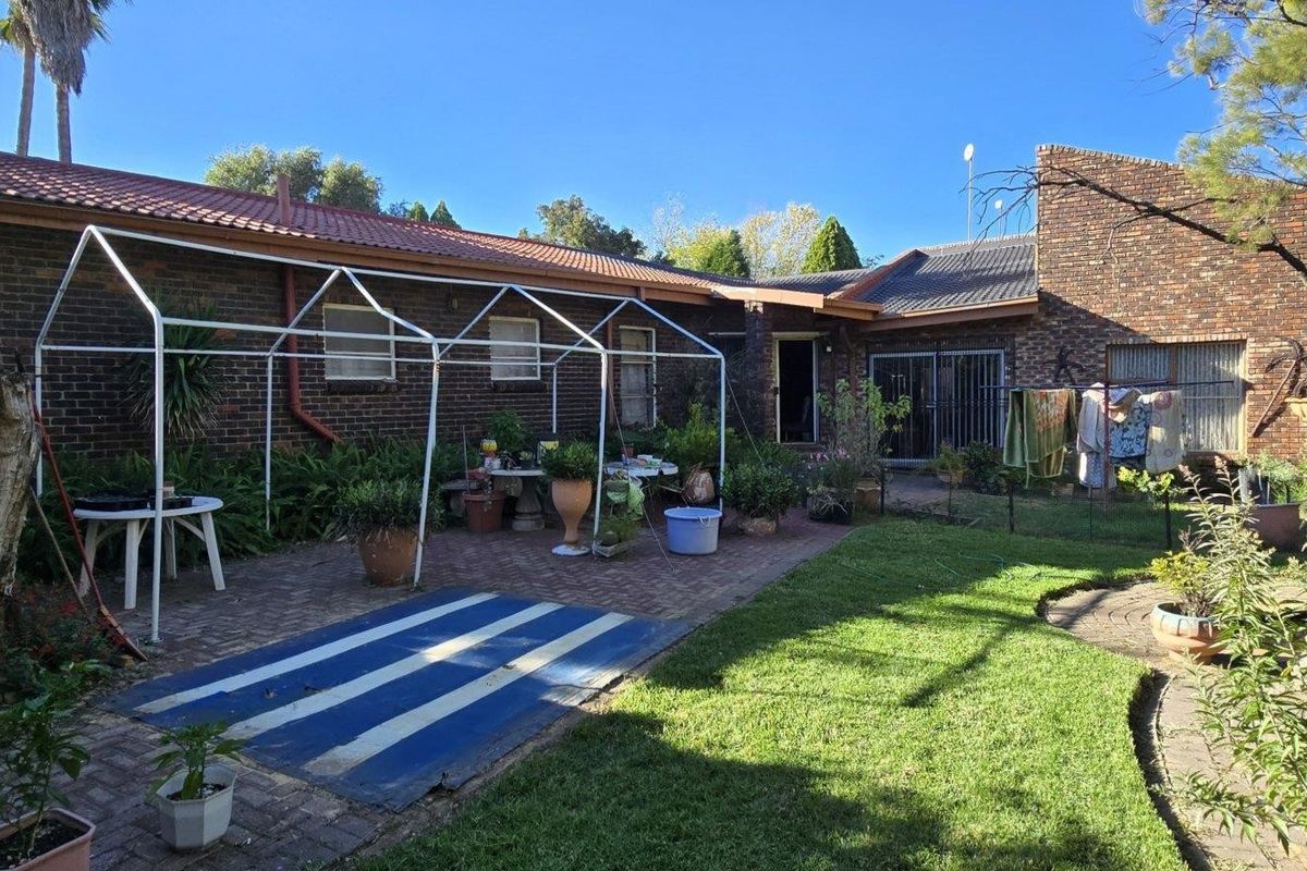 A rear view of the property featuring a brick facade, tiled roof, paved patio area, and a private garden space.