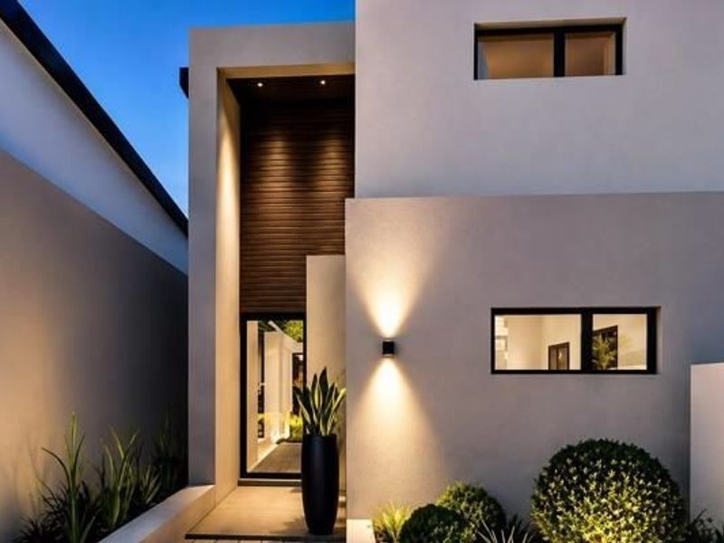 A modern, architecturally designed front facade featuring clean lines, warm accent lighting, timber cladding, and manicured landscaping.
