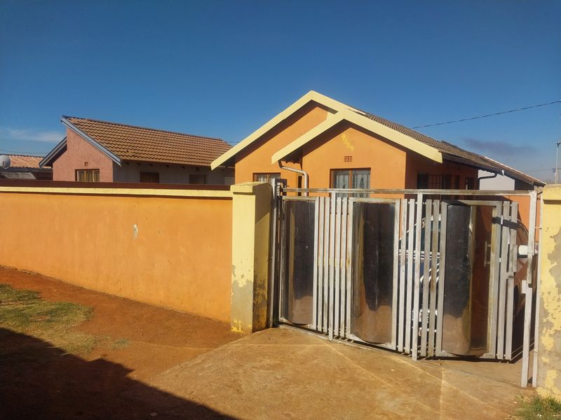 Front view of a residential house featuring a metal sliding gate, perimeter wall, and tiled roof structure.