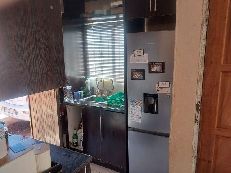 A compact kitchen area featuring dark wood cabinetry, a stainless steel sink, and a window with venetian blinds, showing signs of wear and maintenance needs.