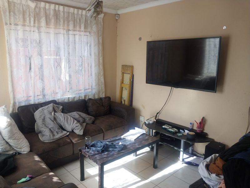 A living room featuring tiled flooring and a window with security bars, currently showing signs of wear on the wall surfaces.