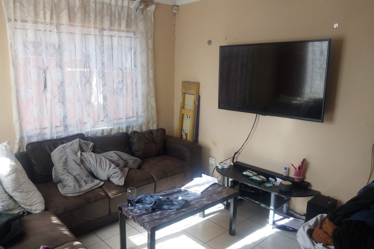 A living room featuring tiled flooring and a window with security bars, currently showing signs of wear on the wall surfaces.