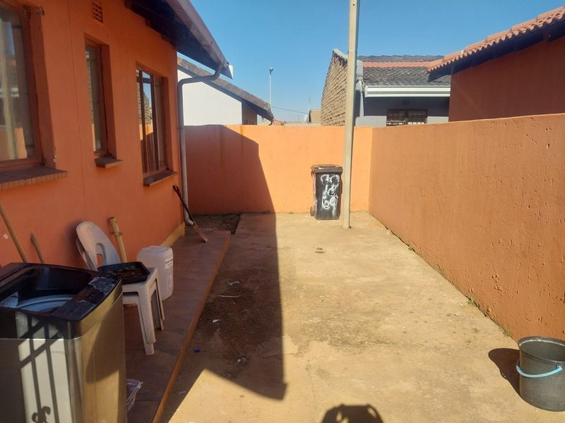 A rear exterior courtyard featuring a concrete paved area, perimeter wall, and a small tiled patio section adjacent to the house.