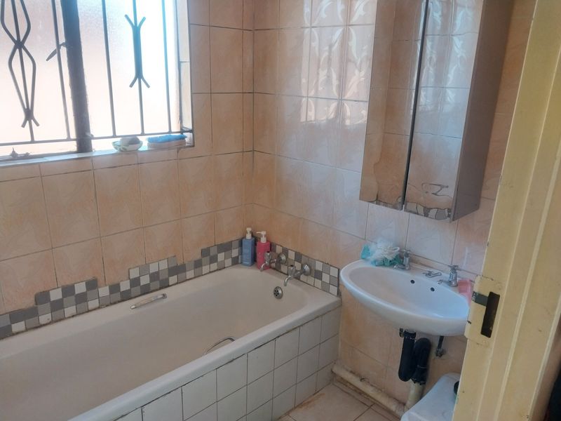 A dated bathroom featuring a standard bathtub, wall-mounted basin, and tiled walls, requiring cosmetic updates to modernize the space.
