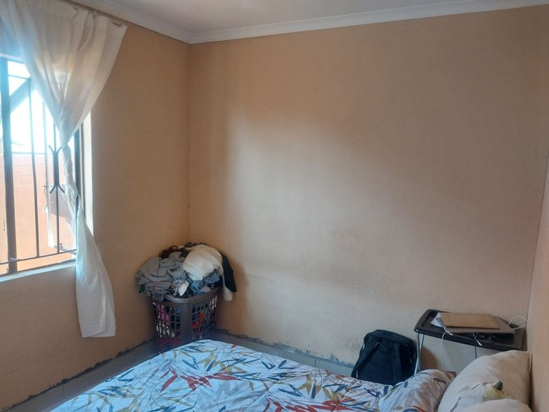 A bedroom featuring a window with security bars and plain wall finishes, requiring cosmetic updates to improve the overall aesthetic.