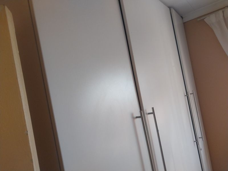 A close-up view of modern white built-in cupboards with stainless steel handles in a bedroom setting.