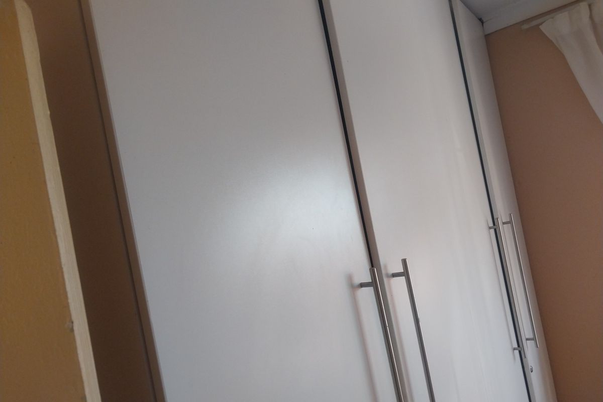 A close-up view of modern white built-in cupboards with stainless steel handles in a bedroom setting.