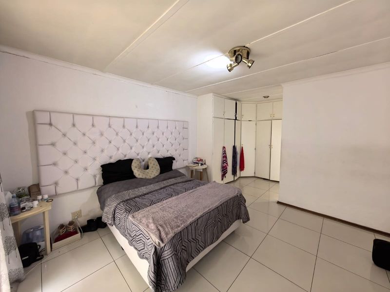 Bedroom featuring tiled flooring, built-in cupboards, and a tufted headboard. The room requires cosmetic updates to the ceiling and finishes.