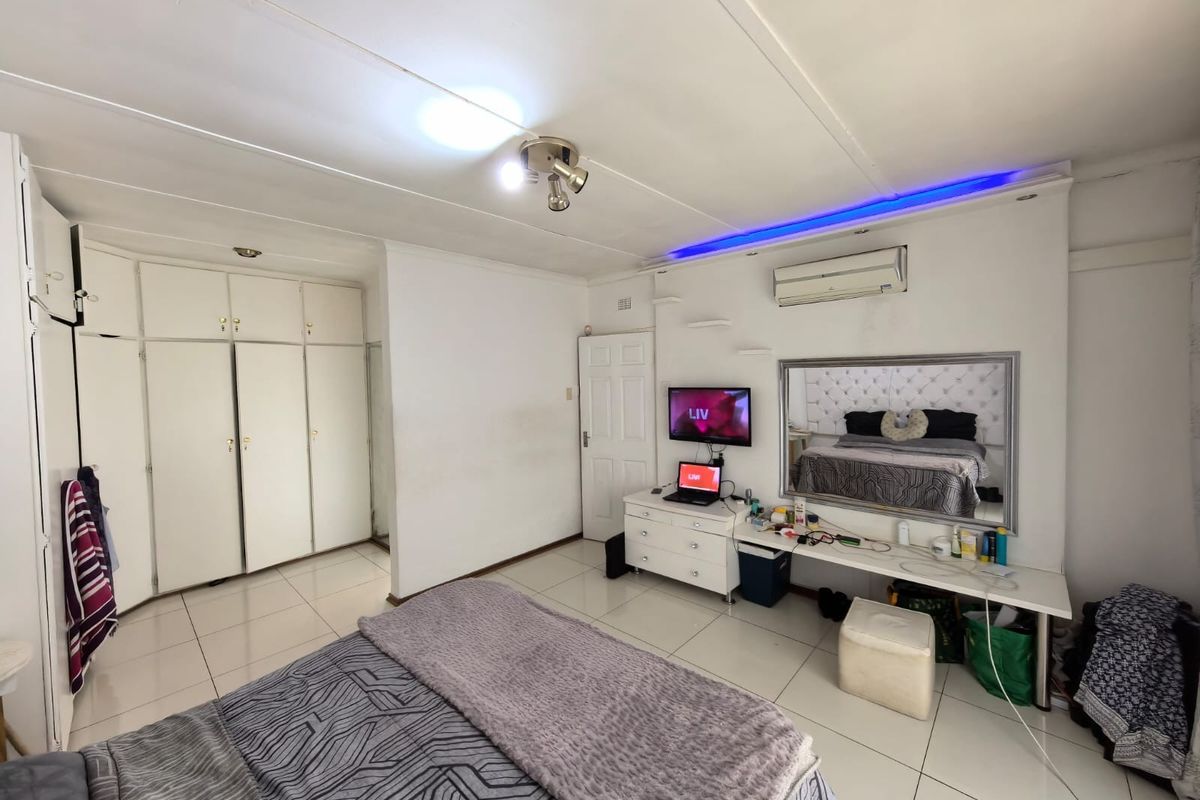 A bedroom featuring tiled flooring, built-in cupboards, a split-system air conditioner, and integrated ceiling lighting.