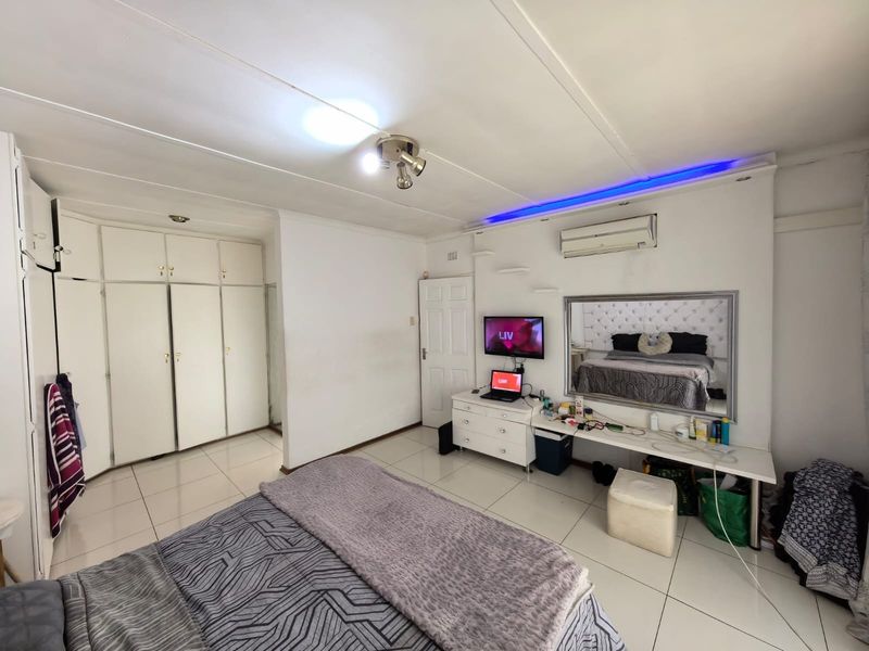 A bedroom featuring tiled flooring, built-in cupboards, a split-system air conditioner, and integrated ceiling lighting.