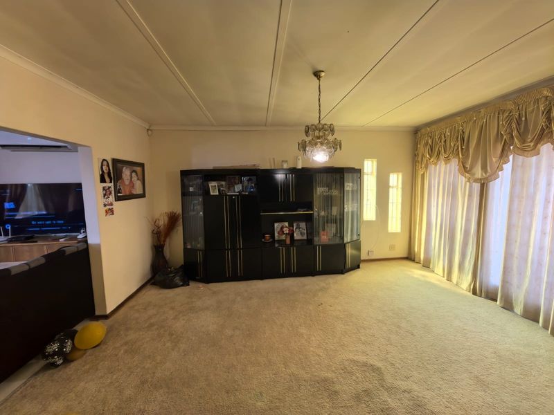 Spacious living room featuring carpeted flooring, a central chandelier, and built-in display cabinetry, offering a traditional layout with potential for modernization.