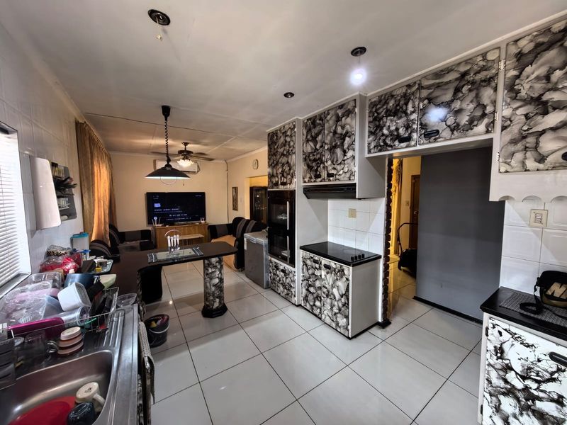 Open-plan kitchen and living area featuring tiled flooring, built-in cabinetry with a unique finish, integrated oven, and hob.