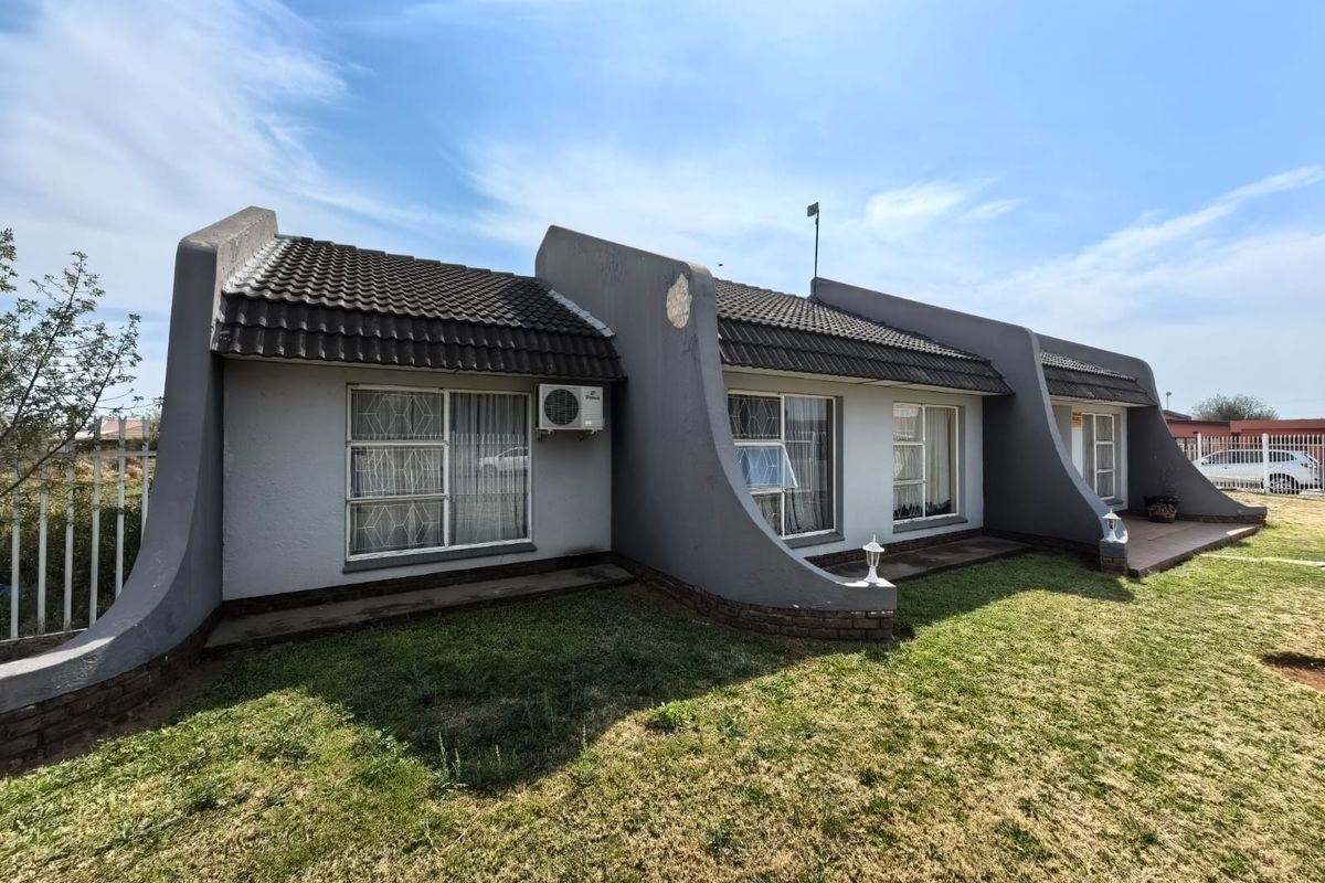 Rear view of a single-story house featuring a tiled roof, security bars on windows, and an installed air conditioning unit with a surrounding lawn area.