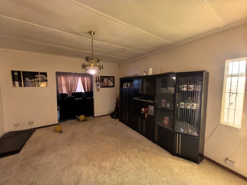 A living room featuring carpeted flooring, a ceiling light fixture, and a window with security bars.