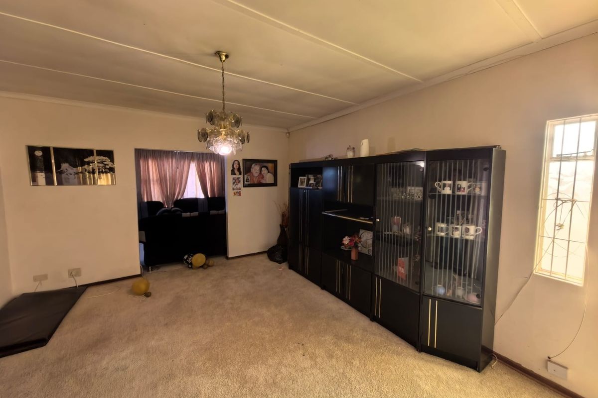 A living room featuring carpeted flooring, a ceiling light fixture, and a window with security bars.