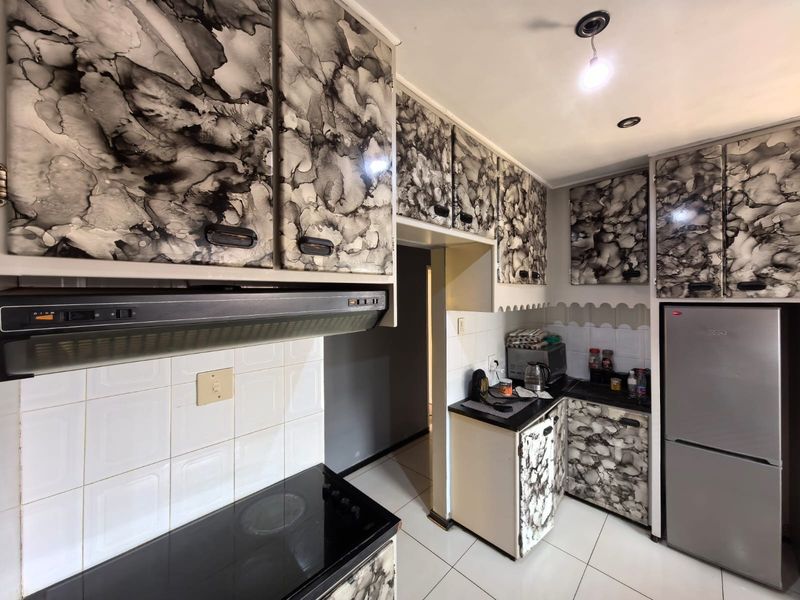 Compact kitchen featuring patterned cabinetry, tiled backsplash, integrated extractor fan, and electric hob with tiled flooring.