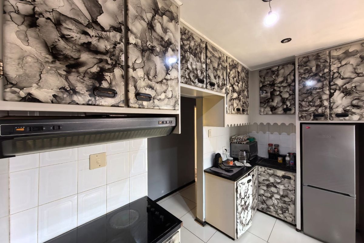 Compact kitchen featuring patterned cabinetry, tiled backsplash, integrated extractor fan, and electric hob with tiled flooring.