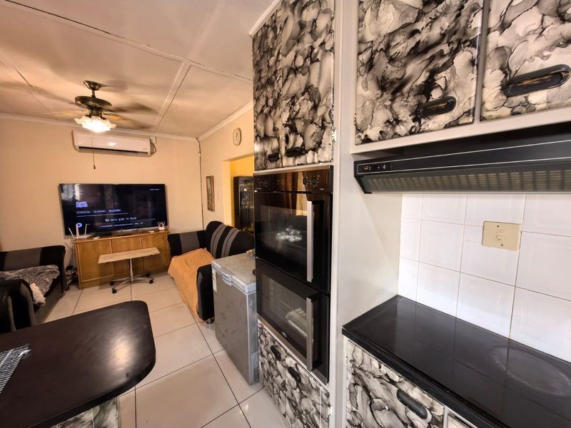 Open-plan living and kitchen area featuring a built-in double oven, ceramic hob, extractor fan, and tiled flooring with a ceiling fan and air conditioning.
