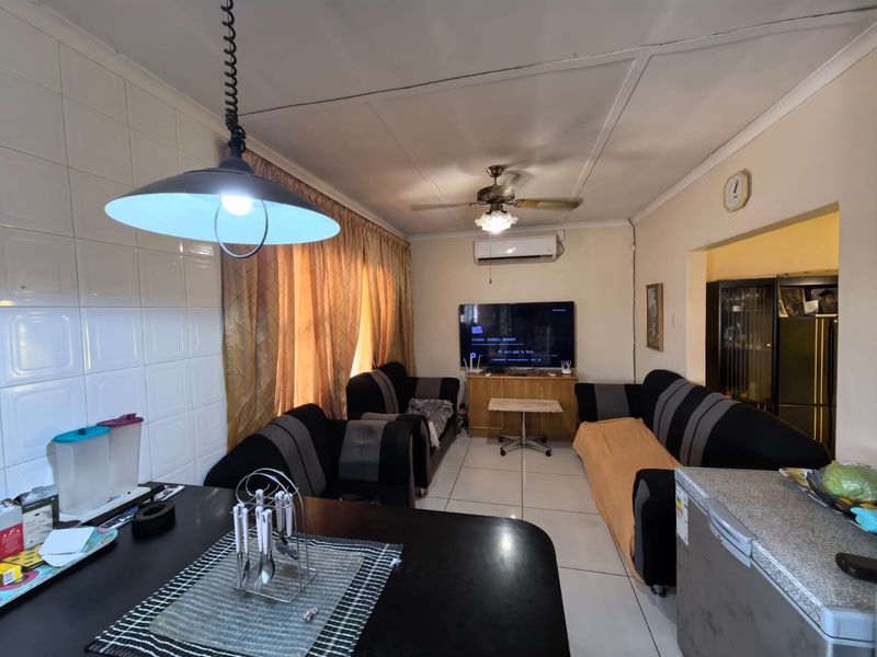 Open-plan living area featuring tiled flooring, ceiling fan, and split-system air conditioning, with a tiled wall section and pendant lighting.