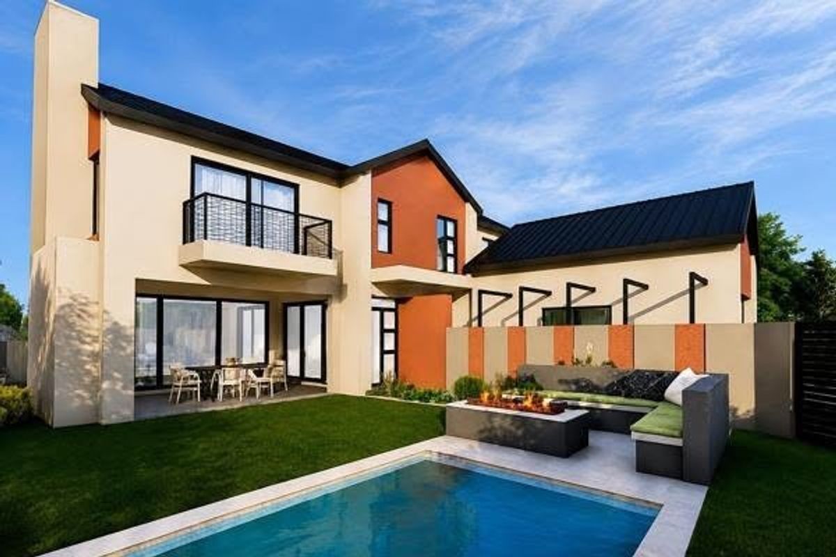 Modern rear exterior featuring a swimming pool, built-in fire pit area, covered patio, and a balcony overlooking the landscaped garden.