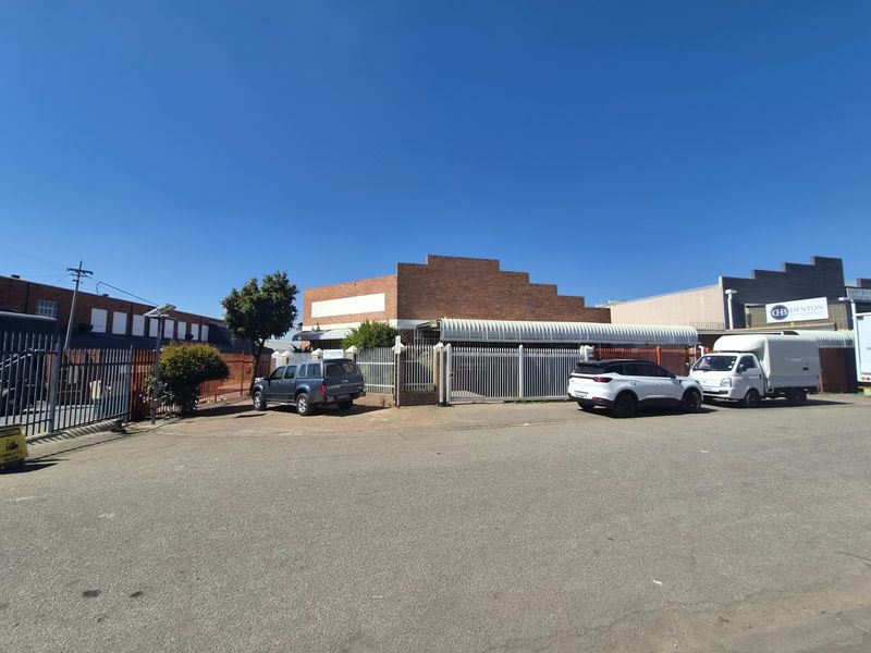 Front exterior view of an industrial property featuring a brick facade, metal security fencing, and a paved driveway area.