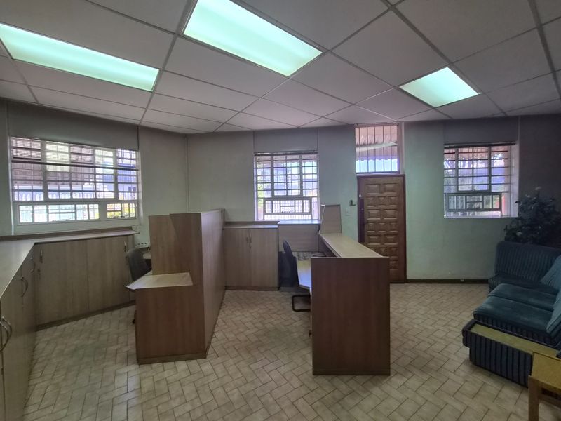 Functional office space featuring a built-in reception desk, extensive cabinetry, suspended ceiling with recessed lighting, and security-barred windows.