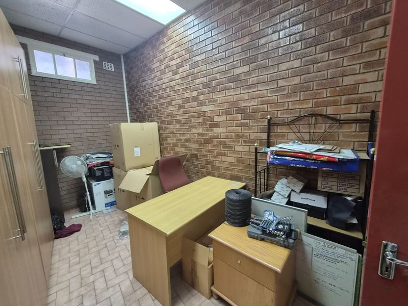 A functional office space featuring exposed brick walls, tiled flooring, and built-in cabinetry, suitable for a workspace or storage area.