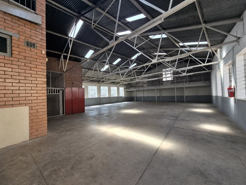 Spacious industrial warehouse featuring high ceilings with exposed steel trusses, skylights, concrete flooring, and a mezzanine level for versatile storage or operational use.