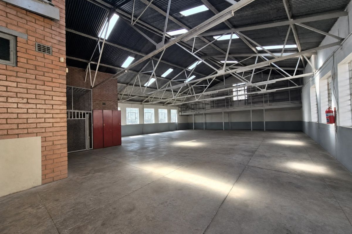 Spacious industrial warehouse featuring high ceilings with exposed steel trusses, skylights, concrete flooring, and a mezzanine level for versatile storage or operational use.