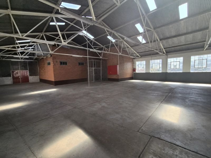 Spacious industrial utility area featuring high exposed steel roof trusses, abundant natural light from skylights, concrete flooring, and secure brick-walled construction.